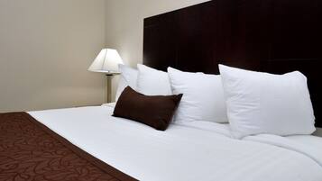 Een hotelkamer met een groot bed, witte beddengoed, een donker hoofdeinde en een bedlamp.