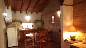 Una cocina acogedora con vigas de madera, una mesa de comedor con sillas, un refrigerador y una pared de piedra.