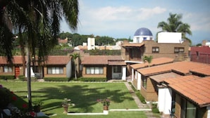 Zona residencial con casas de techo de tejas rojizas, un césped central y un edificio con cúpula al fondo.