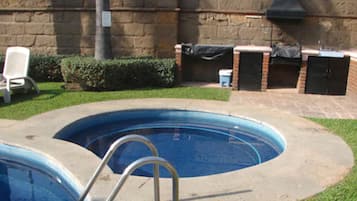 Una piscina con una escalera, zona de barbacoa de ladrillo y una silla blanca.