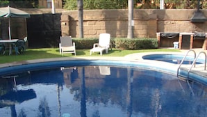 Una piscina con escalera, rodeada por un muro de piedra y un área de césped con mesa y sillas.