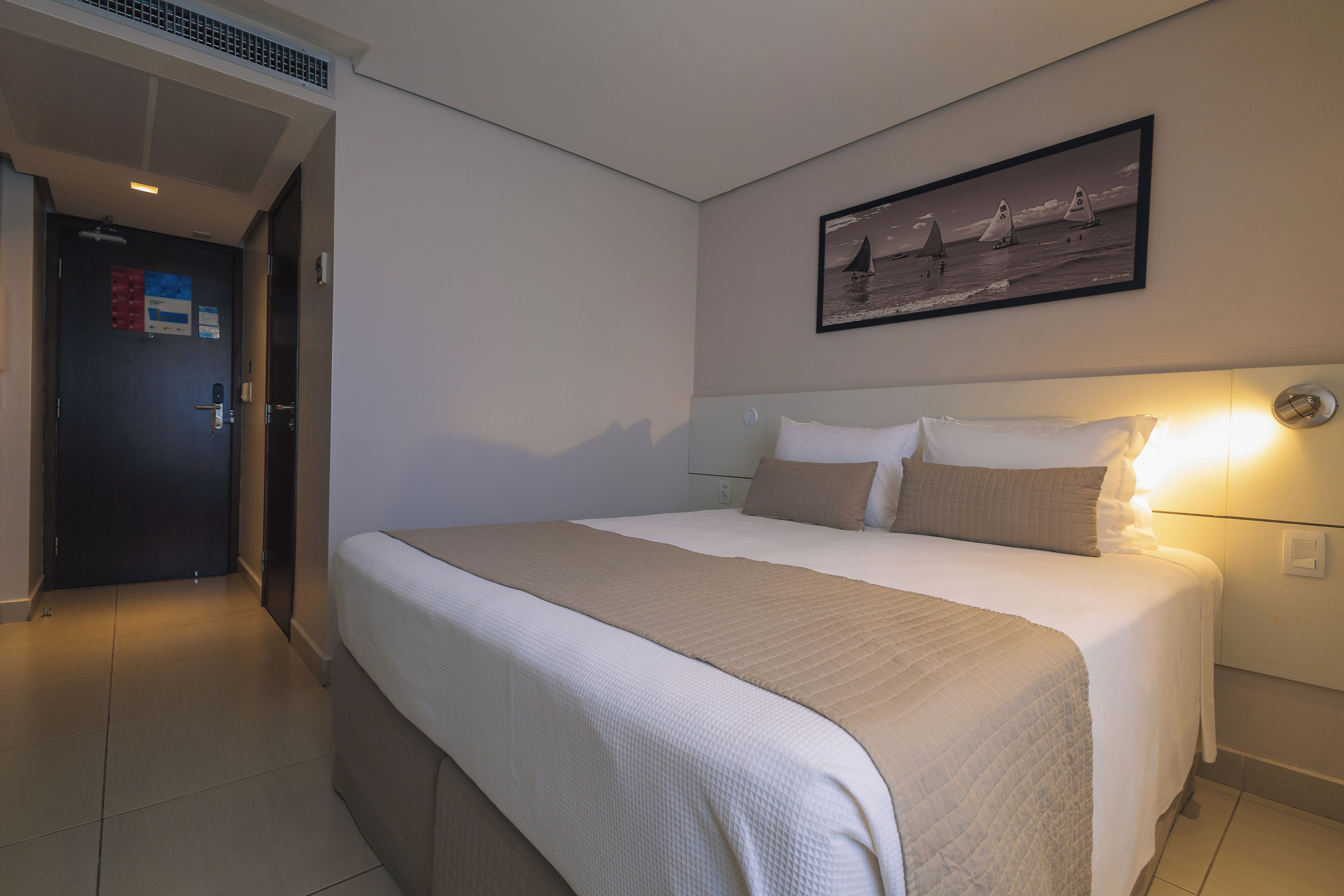 Ein Hotelzimmer mit einem großen Bett, einem Kopfteil, einem Wandbild und einer Tür mit einem Schild.