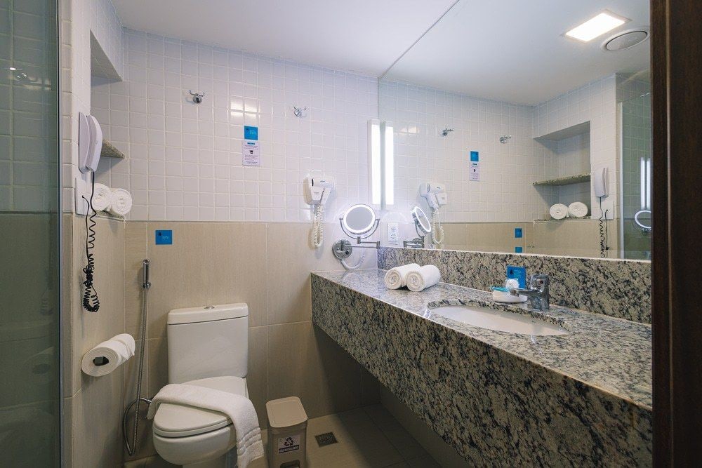 Ein Badezimmer mit Toilette, Waschbecken und Spiegel. Haartrockner und ein Mülleimer sind vorhanden.