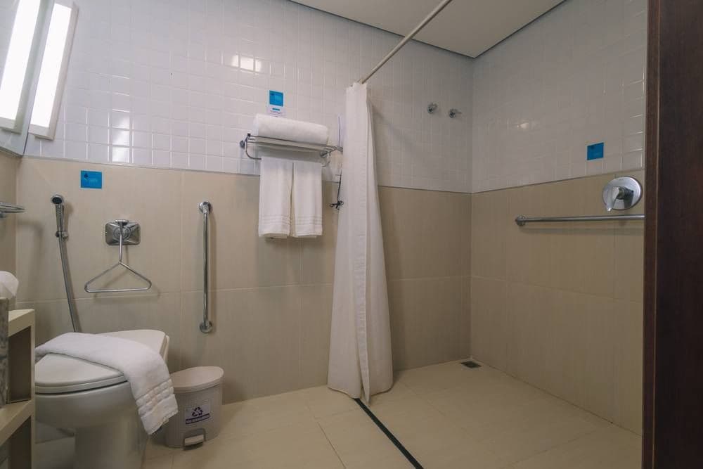 A bathroom with a toilet, a shower, and a handrail.