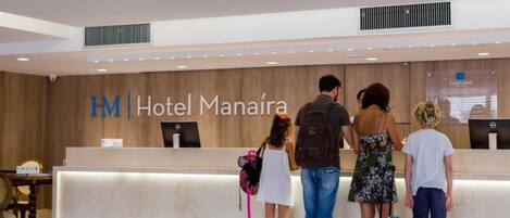 A reception desk at Hotel Manaíra with a wooden wall and a sign.