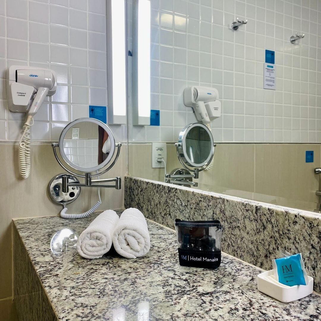 Un baño con encimera de granito, dos secadores de pelo, un espejo, una toalla y un minibar de hotel.