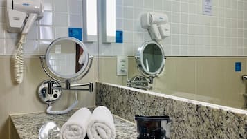 Un baño con encimera de granito, dos secadores de pelo, un espejo, una toalla y un minibar de hotel.