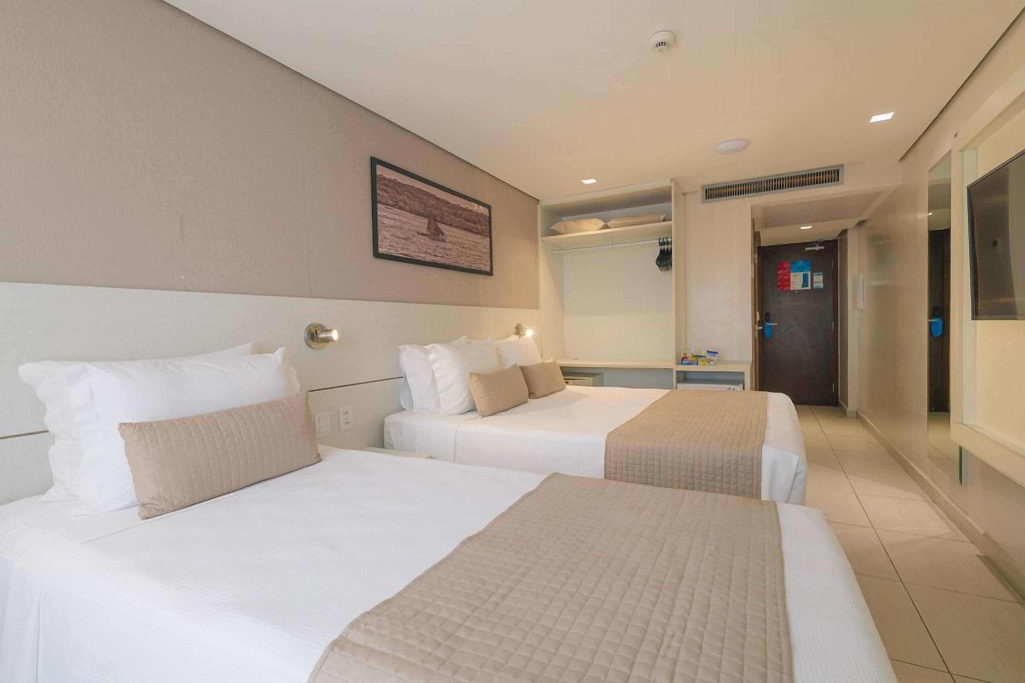 Een hotelkamer met twee bedden, een grote spiegel en een deur naar een gang.