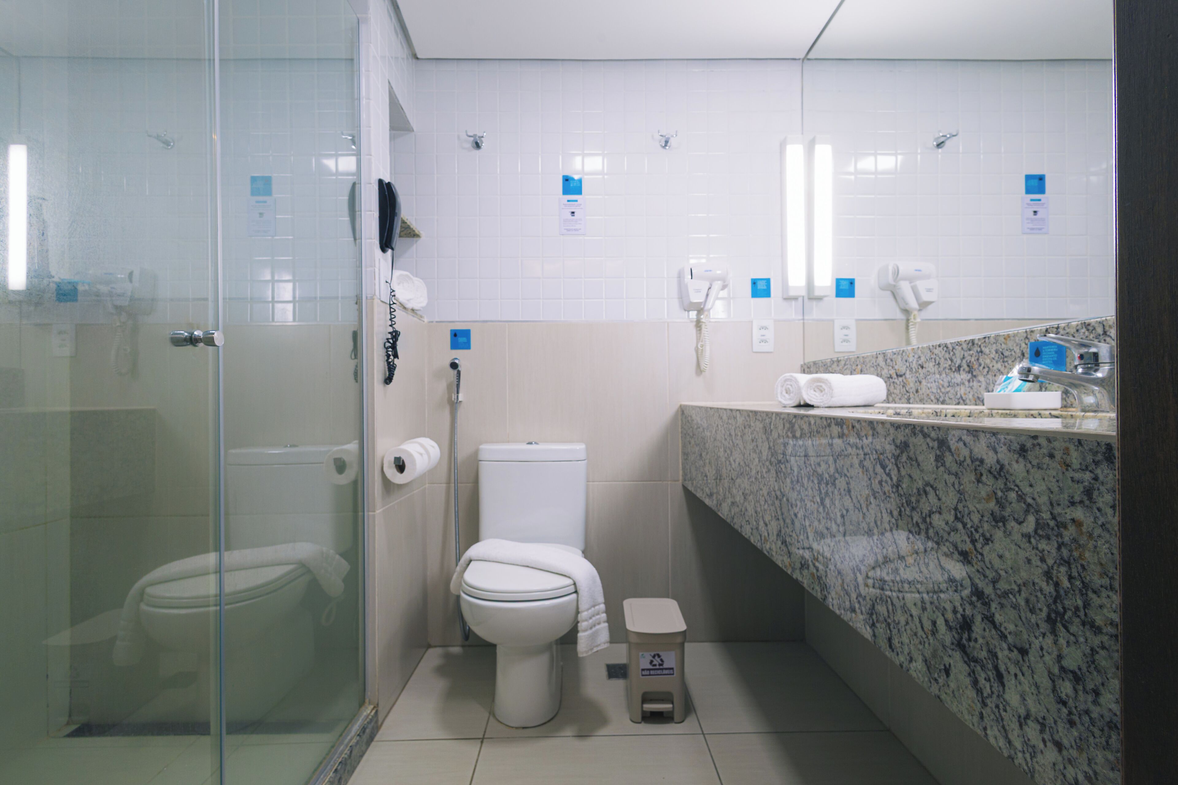 A bathroom with a glass-enclosed shower, a toilet, a sink with a granite countertop, and a trash bin.