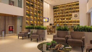 Un vestíbul d'hotel modern amb zones d'estar, una recepció i prestatges decorats amb plantes i objectes ornamentals.