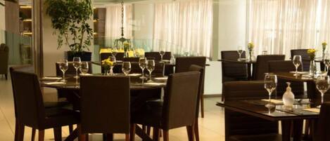 Un restaurante con varias mesas dispuestas para comer, con sillas y copas de vino.