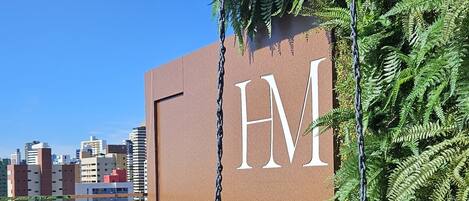 A modern hotel sign with 'HM' prominently displayed, surrounded by lush greenery and potted plants on a rooftop terrace.