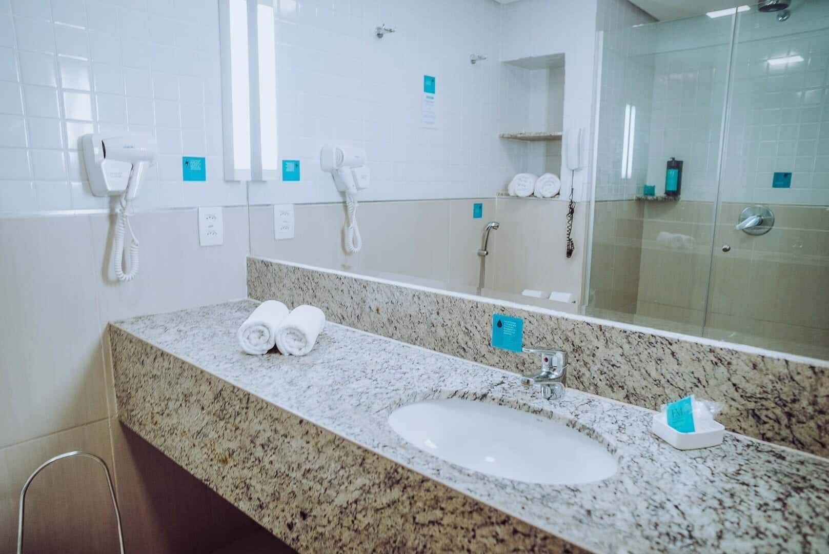A hotel bathroom with a granite countertop sink, two towels, a mirror, and a glass-enclosed shower area.