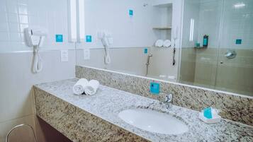 Baño de hotel con lavamanos de encimera de granito, dos toallas, un espejo y cabina de ducha con paredes de vidrio.