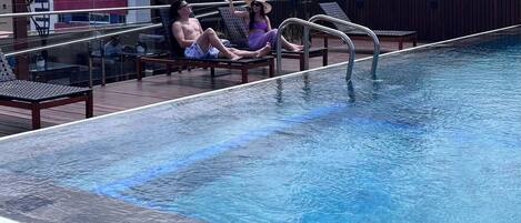 En pool på taket med utsikt över staden, solstolar och en bar.