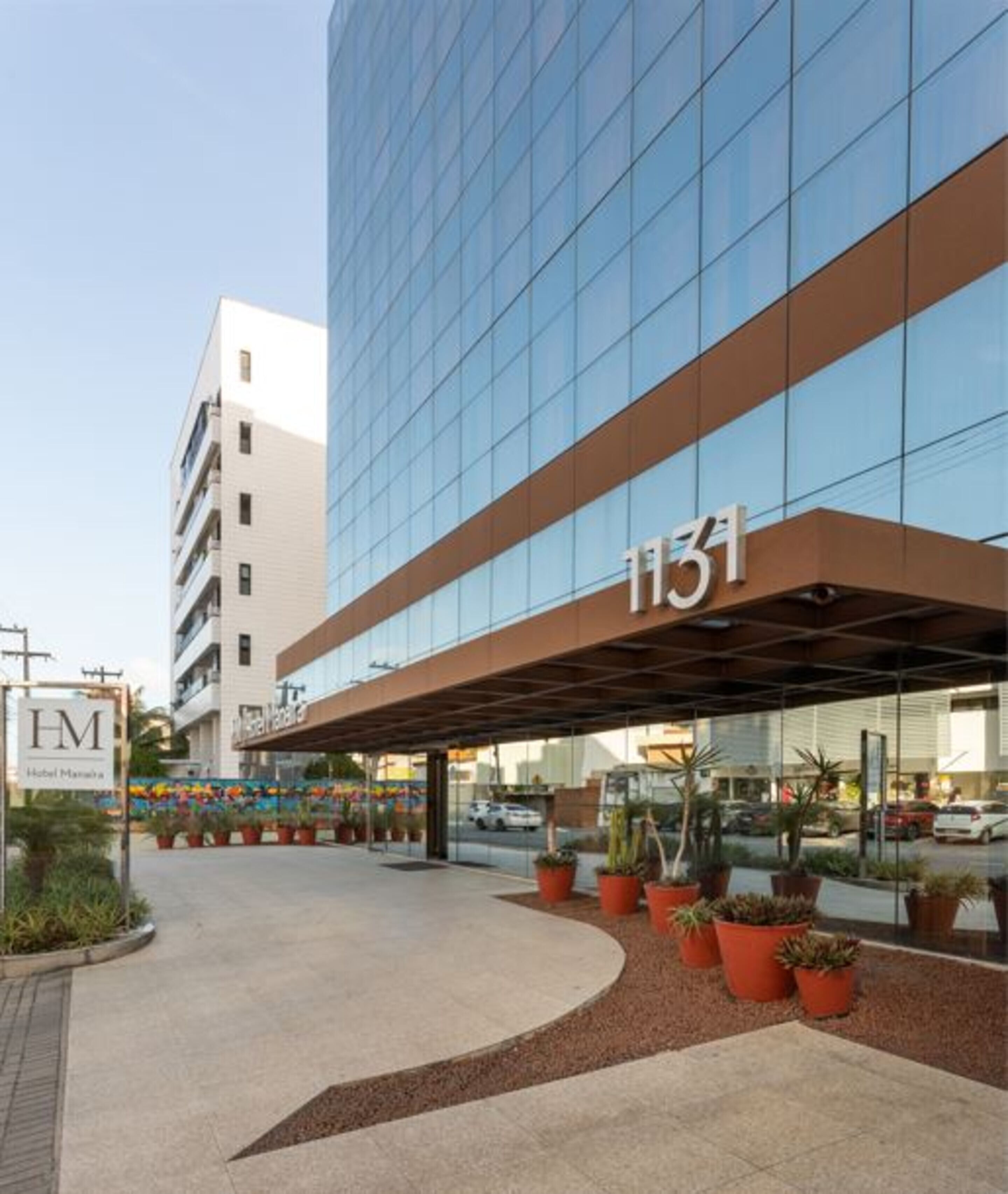Una entrada de hotel moderna con fachada de vidrio, número 1131, y un área de acceso cubierta con plantas en macetas.