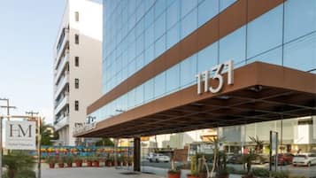 Una entrada de hotel moderna con fachada de vidrio, número 1131, y un área de acceso cubierta con plantas en macetas.