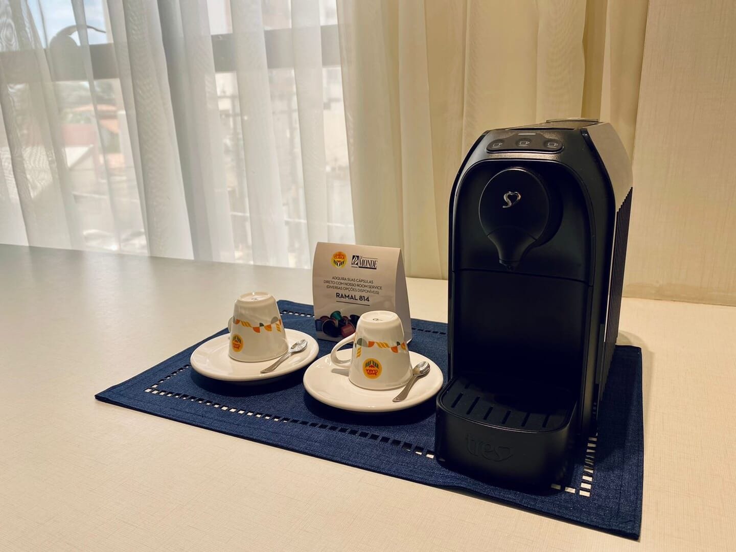 A coffee maker on a table with two cups and a sign.