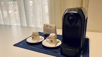 A coffee maker on a table with two cups and a sign.