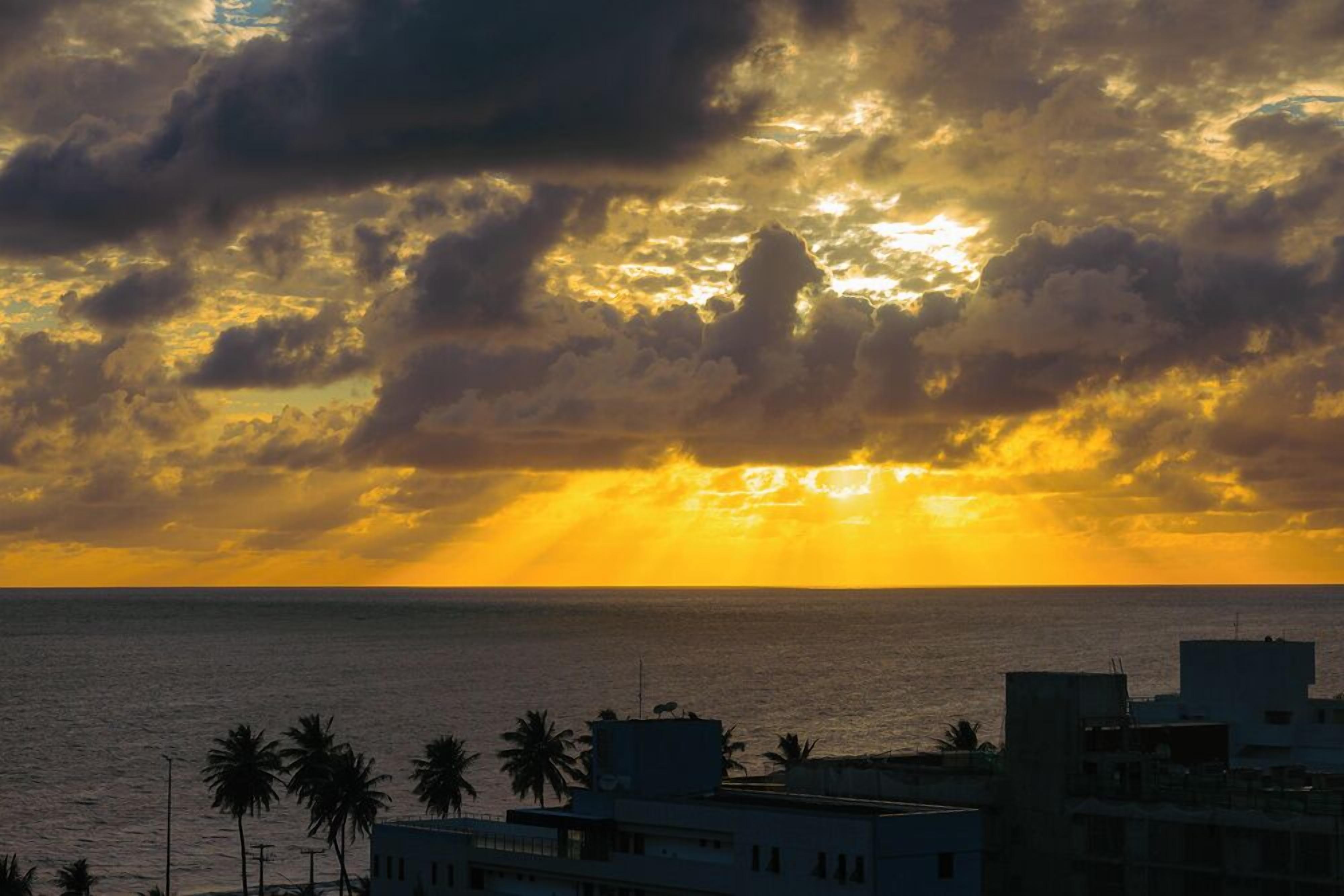 A coastal sunset with buildings and palm trees in the foreground.