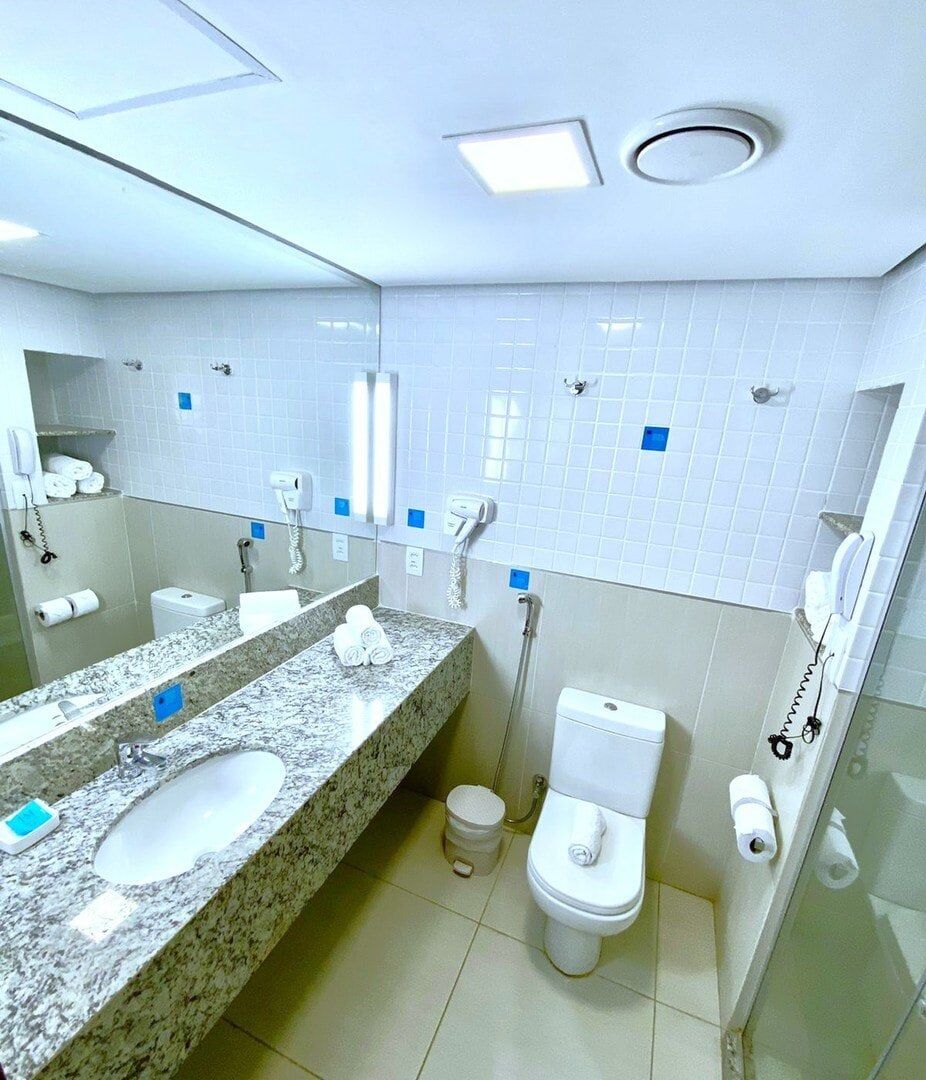A modern bathroom with a granite countertop, two sinks, a toilet, and a shower area.