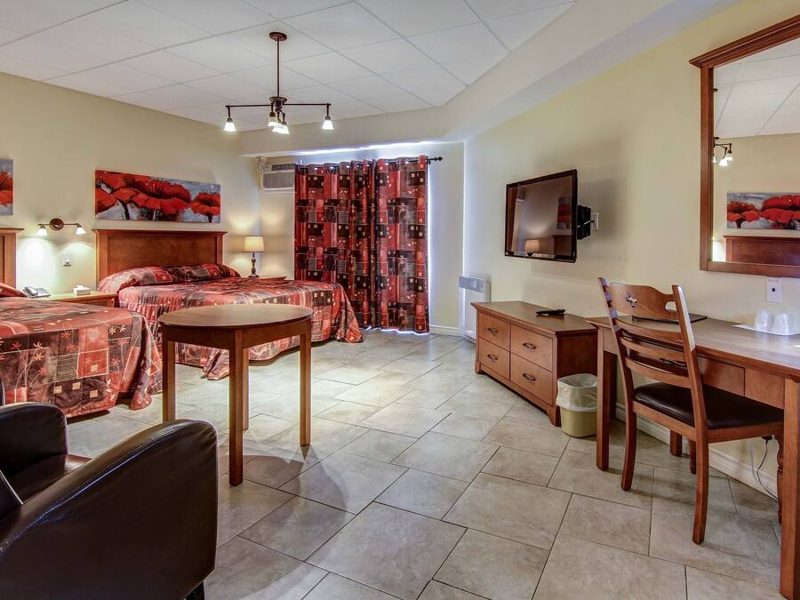 Habitación de hotel con dos camas, un escritorio, una silla, una mesa, un espejo y obras de arte en las paredes.