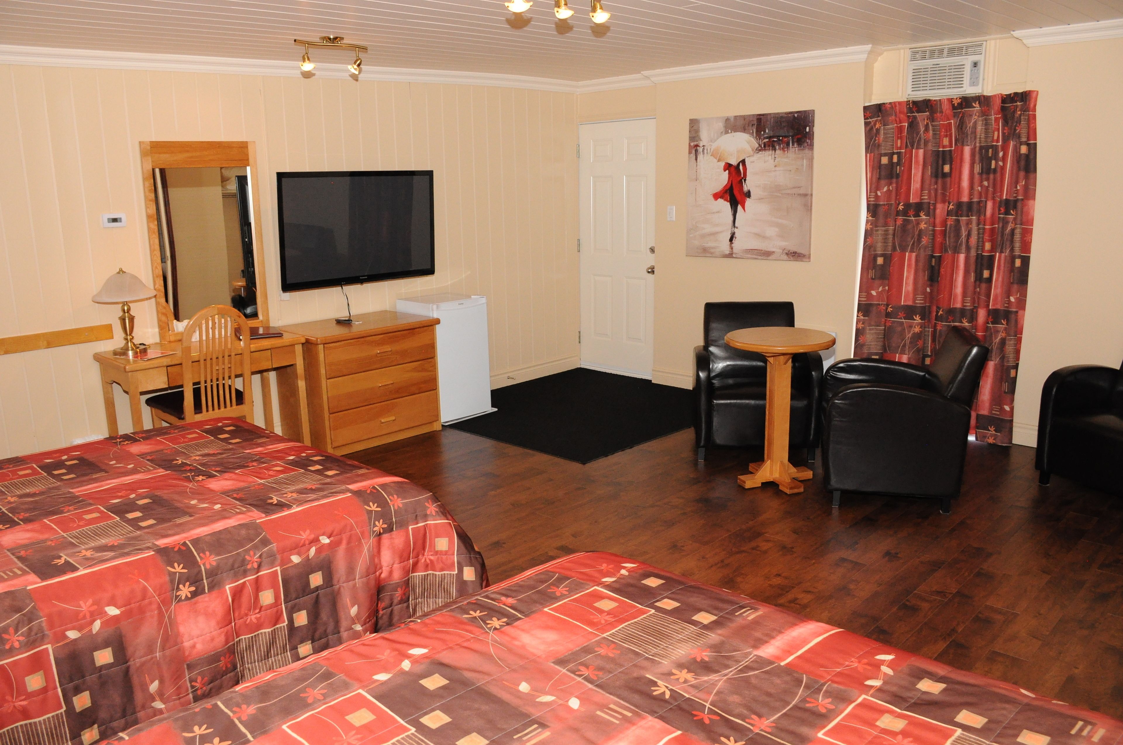 A hotel room with two beds, a desk, a television, a chair, and a small table.
