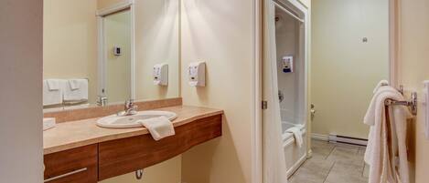 A bathroom with a sink, mirror, towel rack, and a shower area visible through an open door.