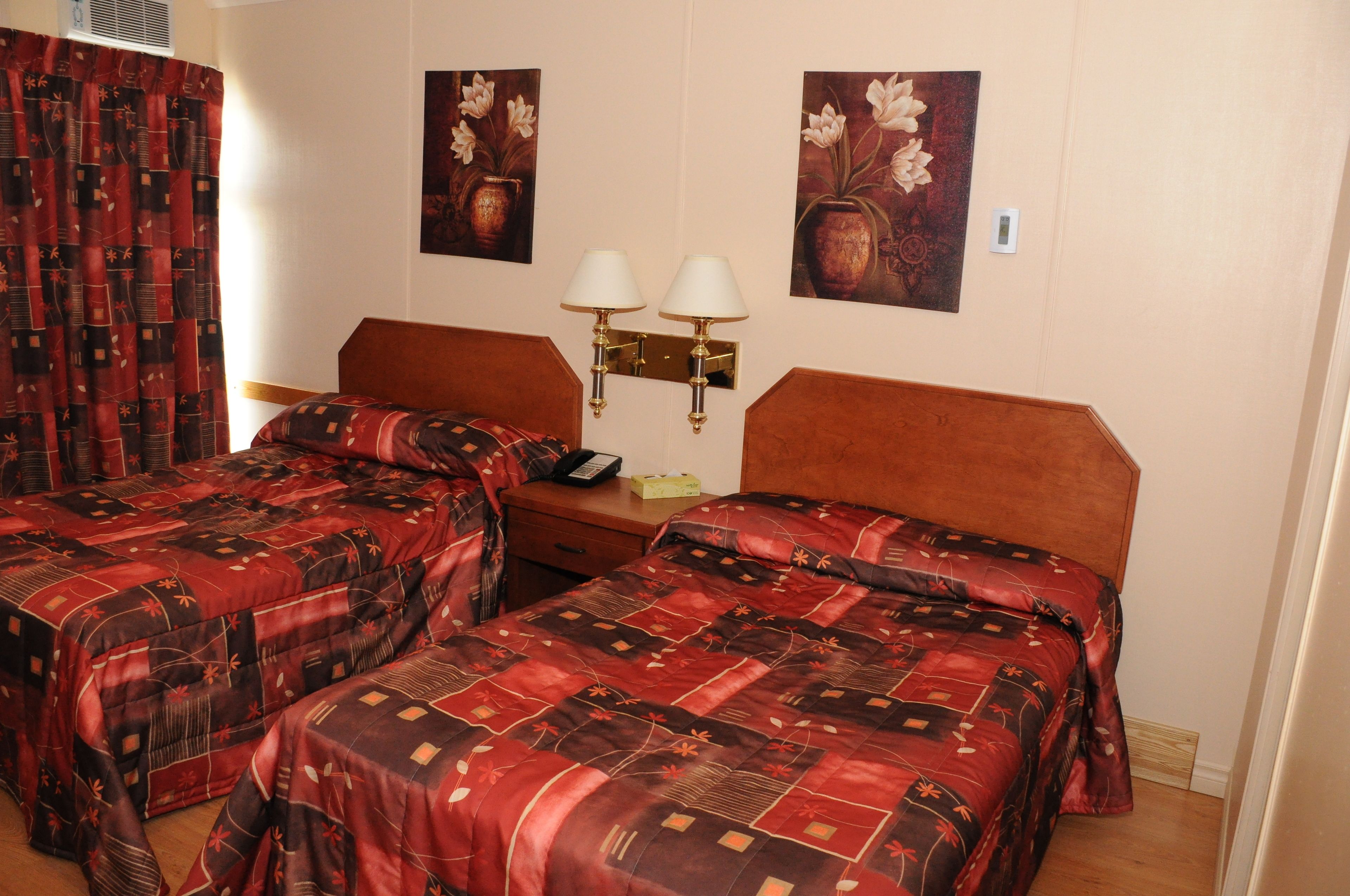 Een hotelkamer met twee bedden, een houten hoofdbord, een nachtkastje met een lamp en twee wandlampen.