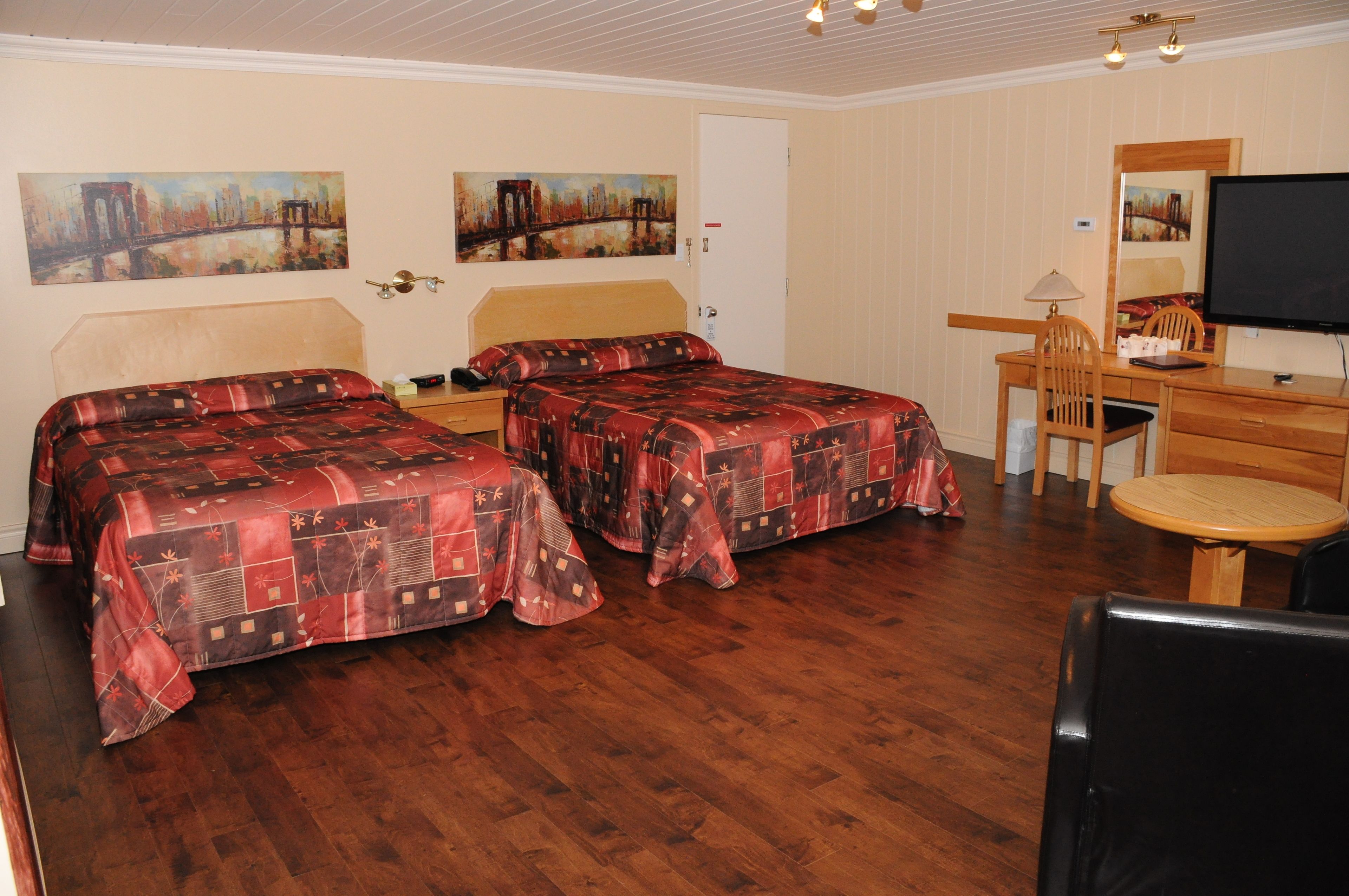 Habitación de hotel con dos camas, un escritorio, una silla, televisión y obras de arte en las paredes.