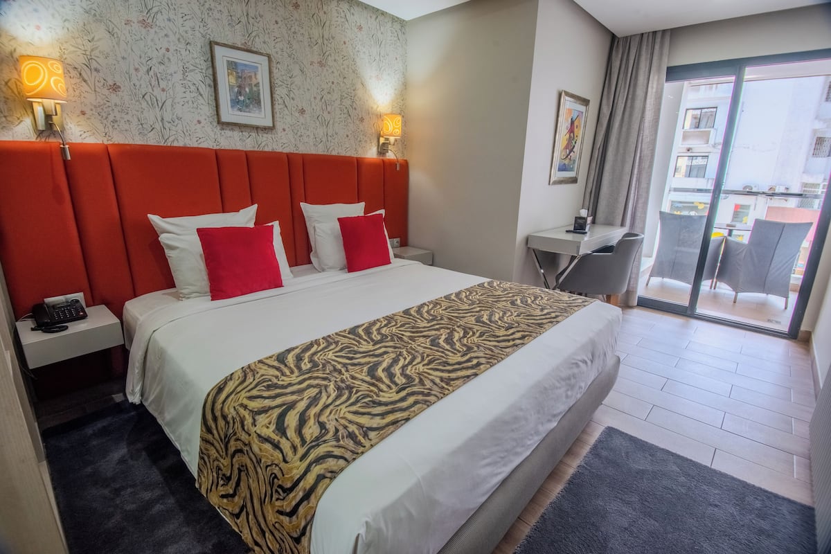 Ein Hotelzimmer mit einem großen Bett, einem Schreibtisch, einem Stuhl, einem Telefon auf dem Nachttisch und Blick auf den Balkon.