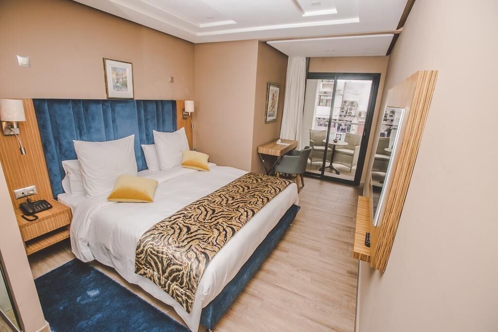 A hotel room with a large bed, a desk, and a view of the city through the window.