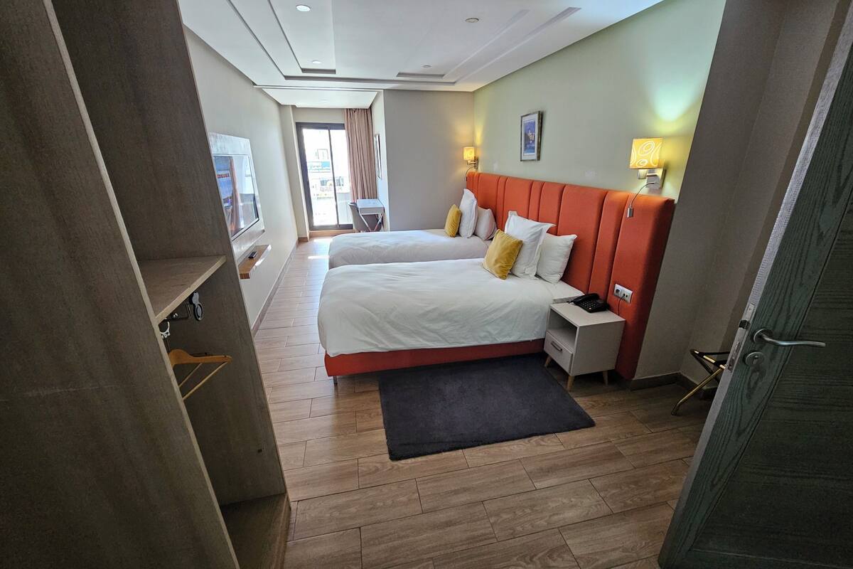 Ein Hotelzimmer mit zwei Betten, einem Schreibtisch, einem Stuhl, einem Fernseher und einer Tür.
