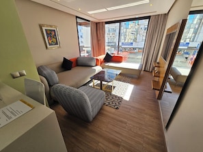 Uma sala de estar moderna com um sofá, poltronas, uma mesa de centro e vista para a cidade através de grandes janelas.