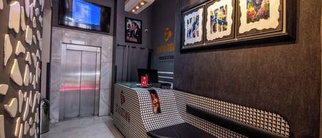 A hotel reception area with a modern design, including a reception desk, a digital screen, and framed artwork on the wall.