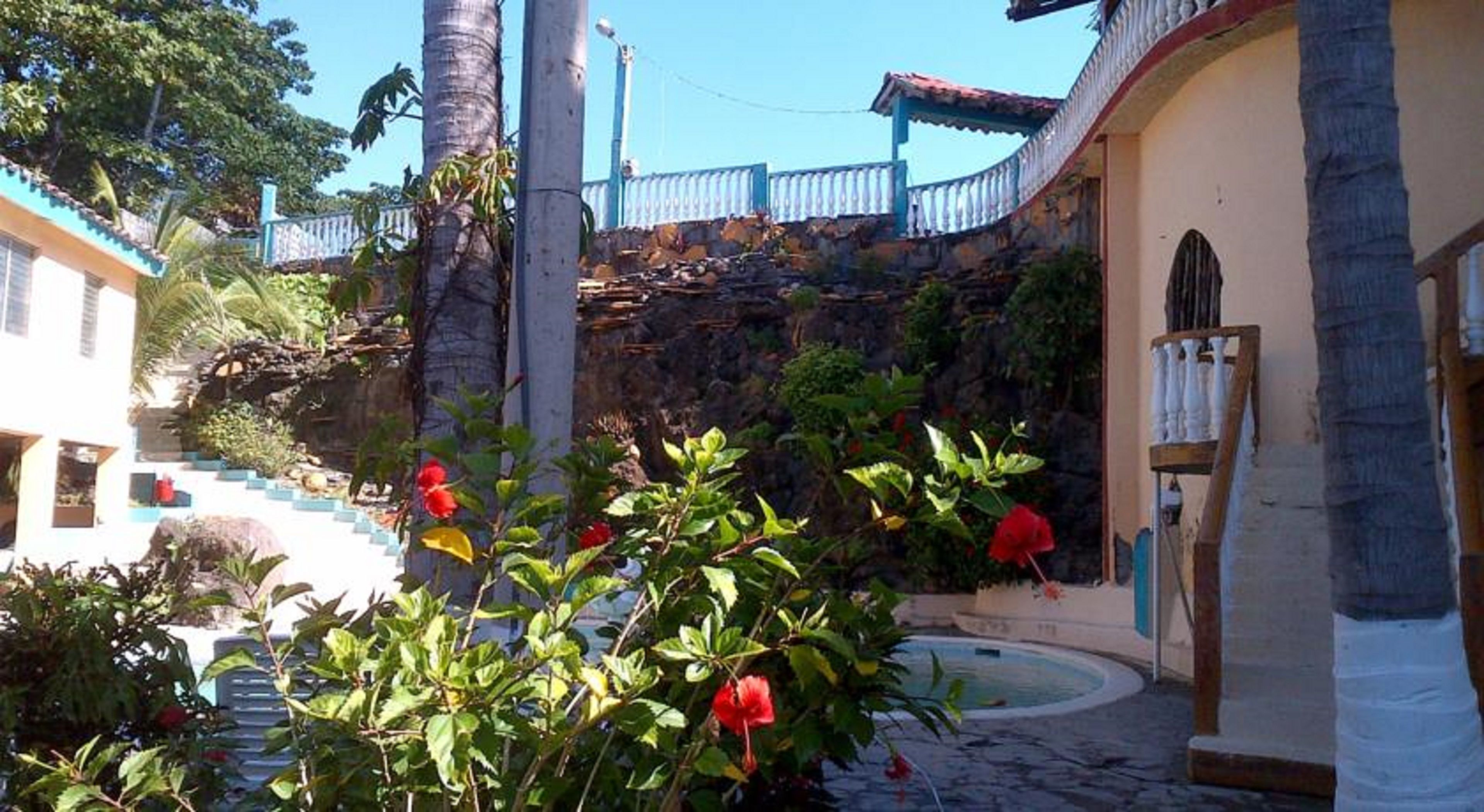 Un patio con piscina, palmeras y una escalera que lleva a un edificio con barandilla azul.