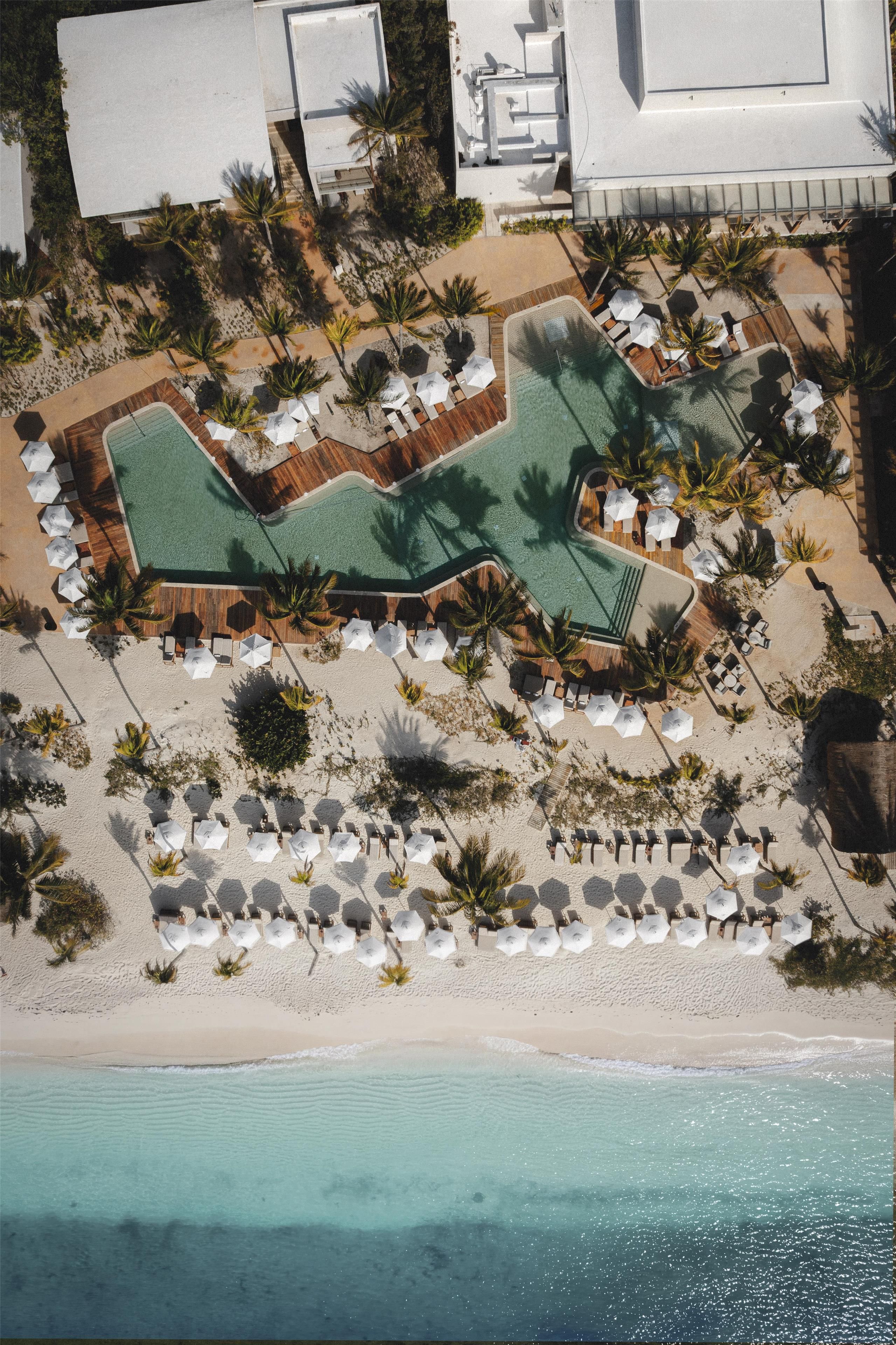 Vista aérea de un resort con piscina, zona de playa y sillas de descanso.