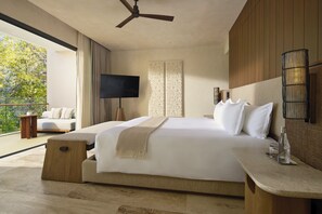 Une chambre d’hôtel moderne dotée d’un grand lit, d’un téléviseur à écran plat, d’un ventilateur de plafond et d’un balcon offrant une vue sur les arbres.