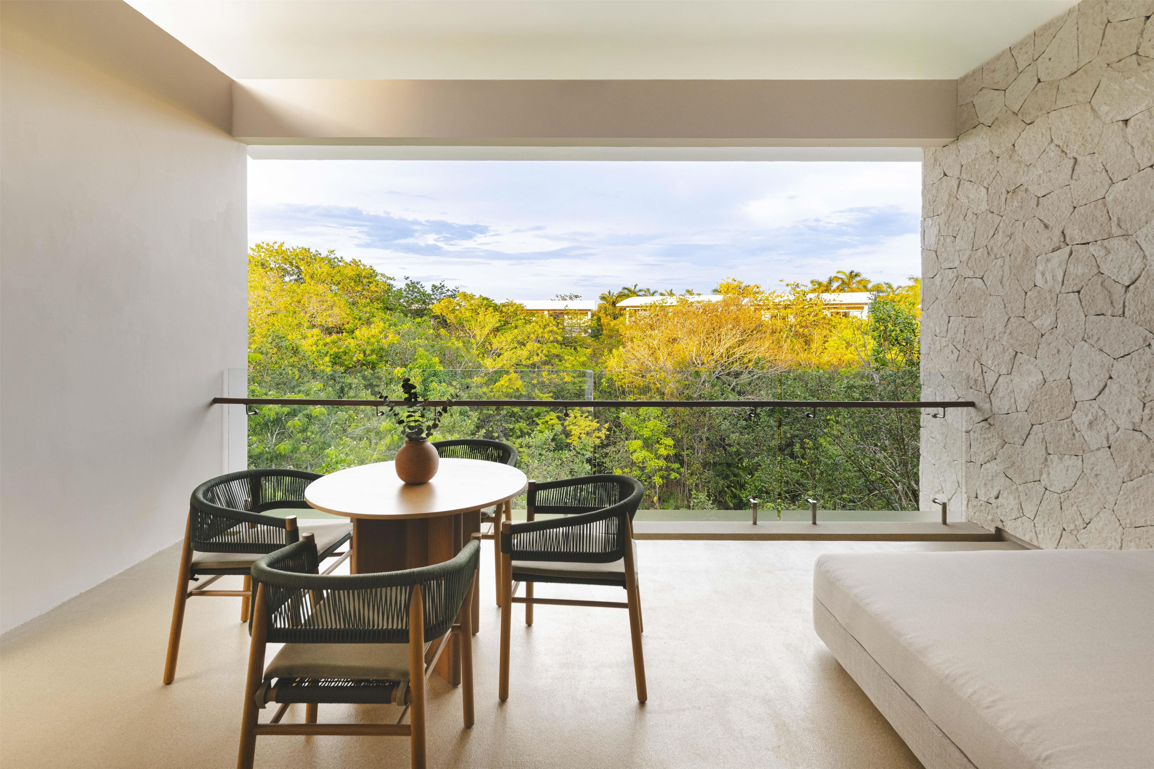 Un balcon avec une table et des chaises, une vue sur les arbres et un mur en pierre.