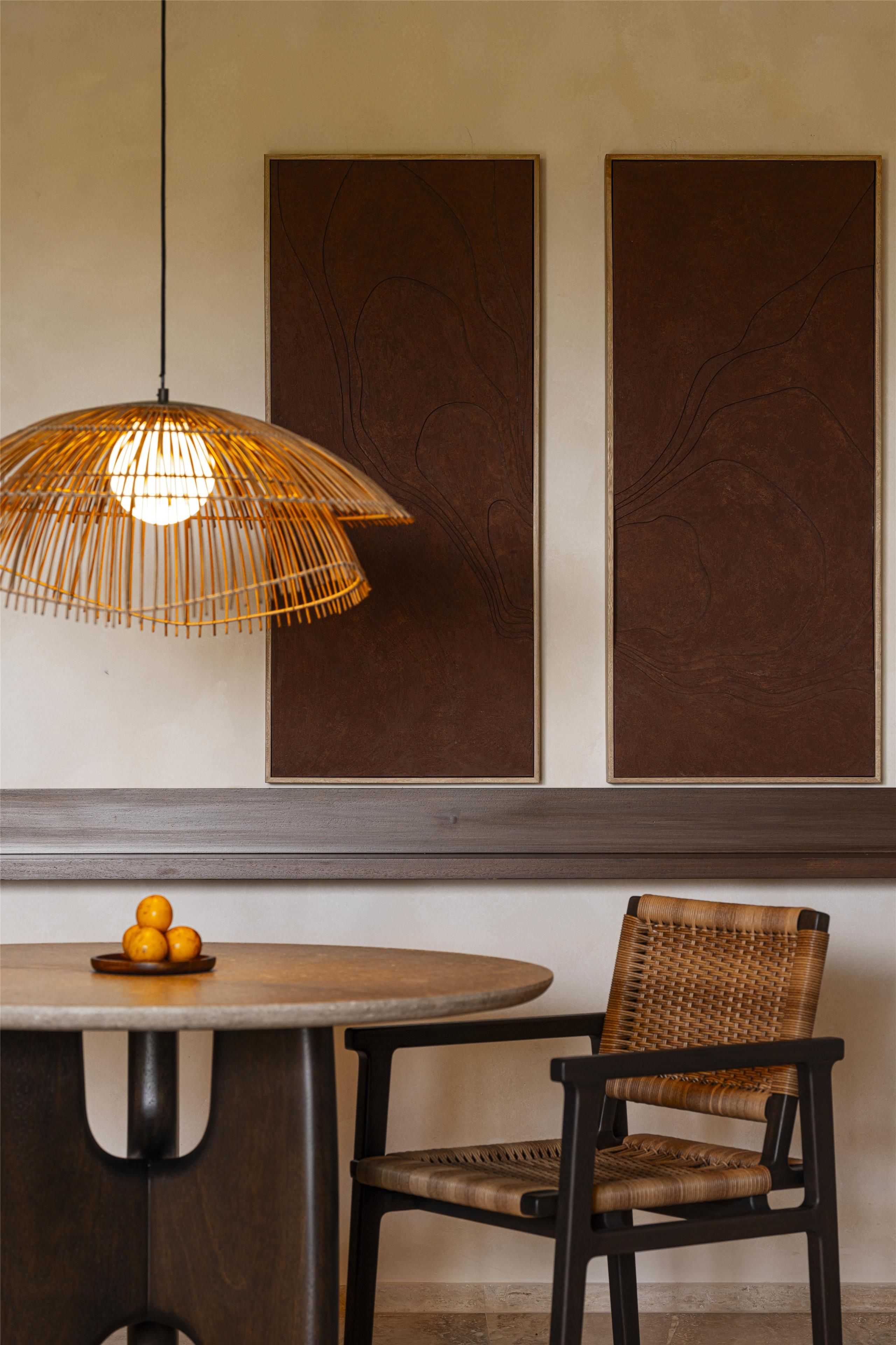 A dining area with a round table, a wicker chair, and a hanging light fixture.