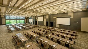 Une salle de conférence avec des rangées de tables et de chaises, de grandes fenêtres et un plafond haut doté d’un système d’éclairage linéaire.