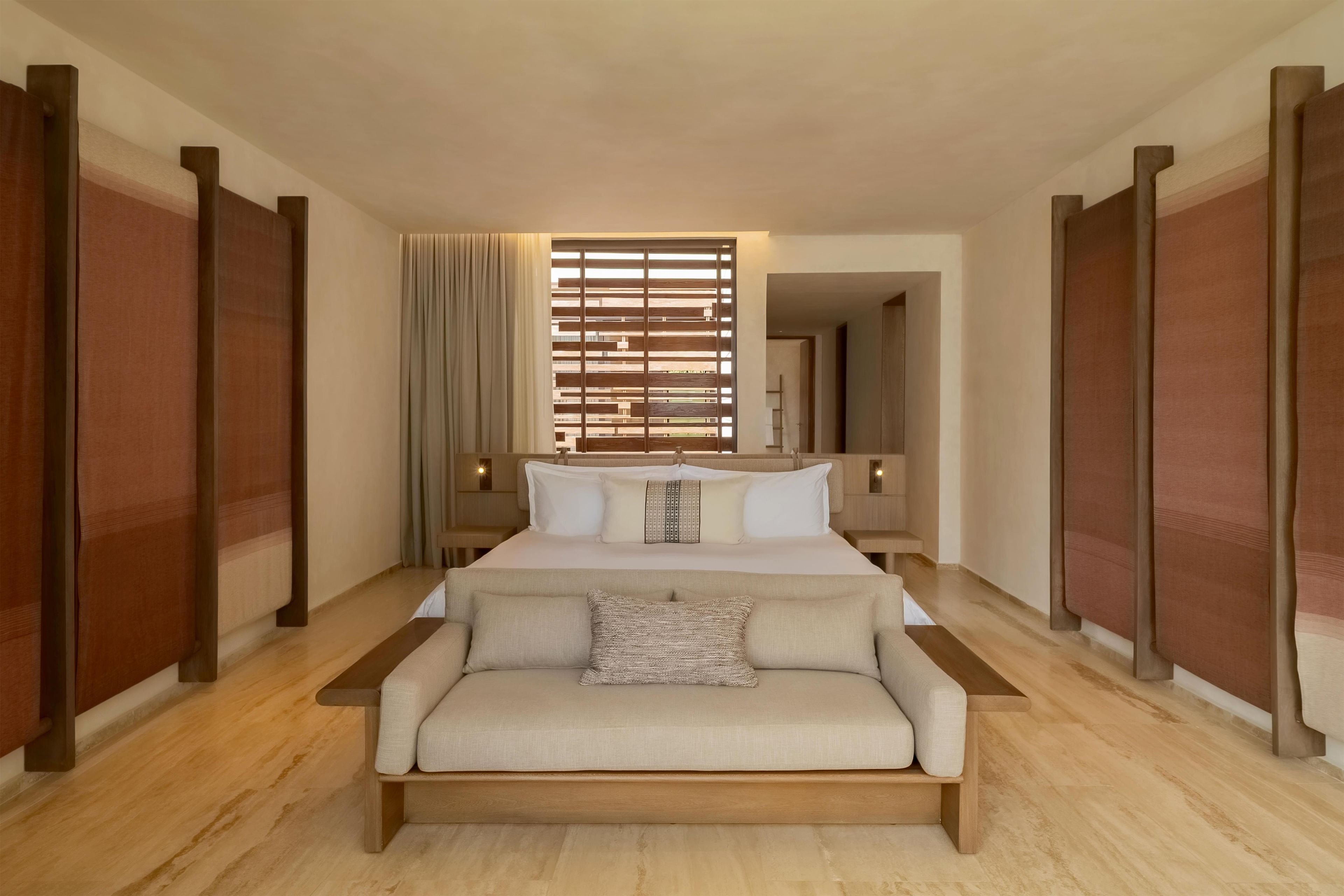 Een hotelkamer met een groot bed, een slaapbank, een raam met zonwering en een spiegel aan de muur.