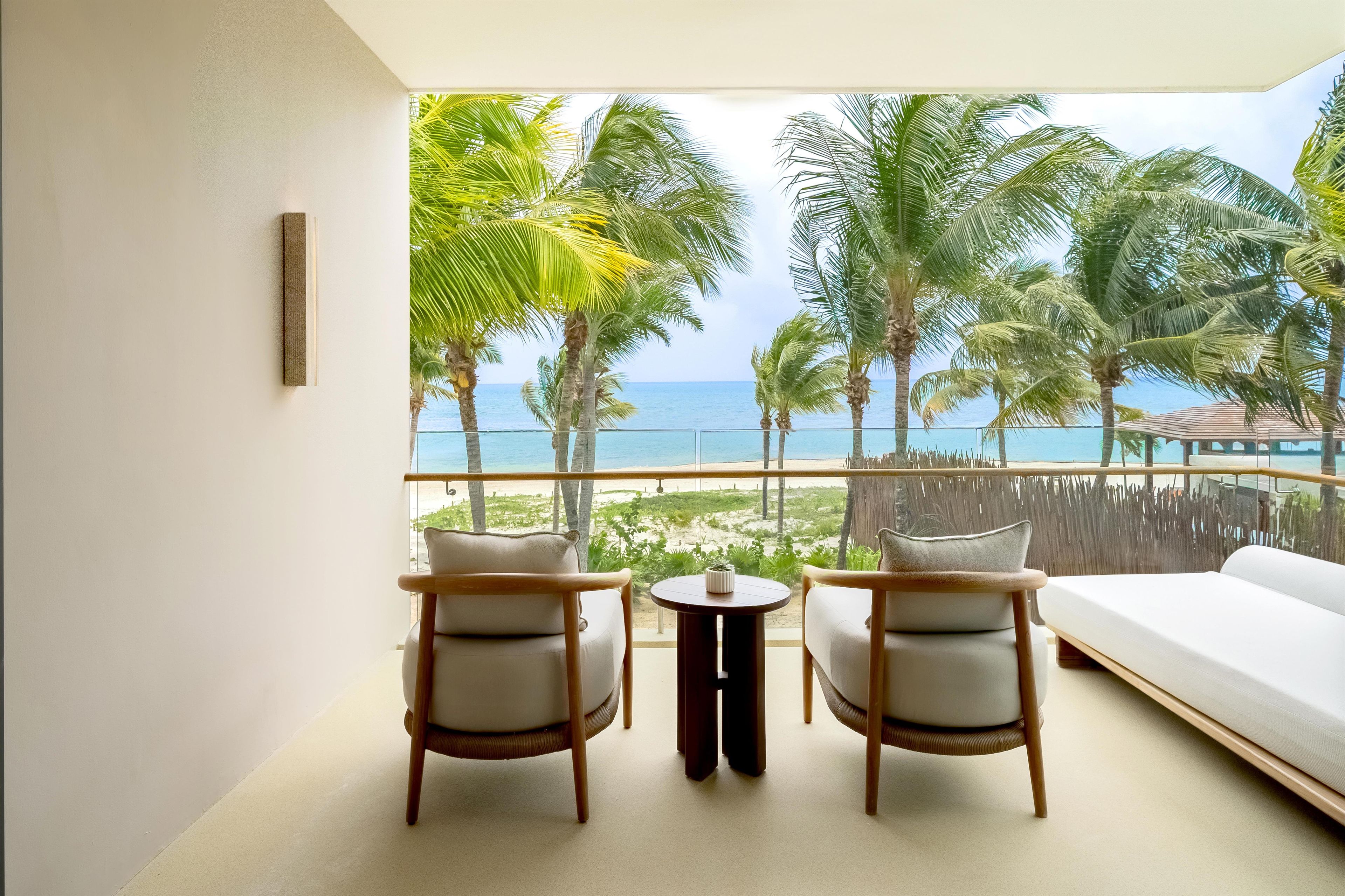 A balcony with a view of the beach and ocean, furnished with a sofa and two chairs.