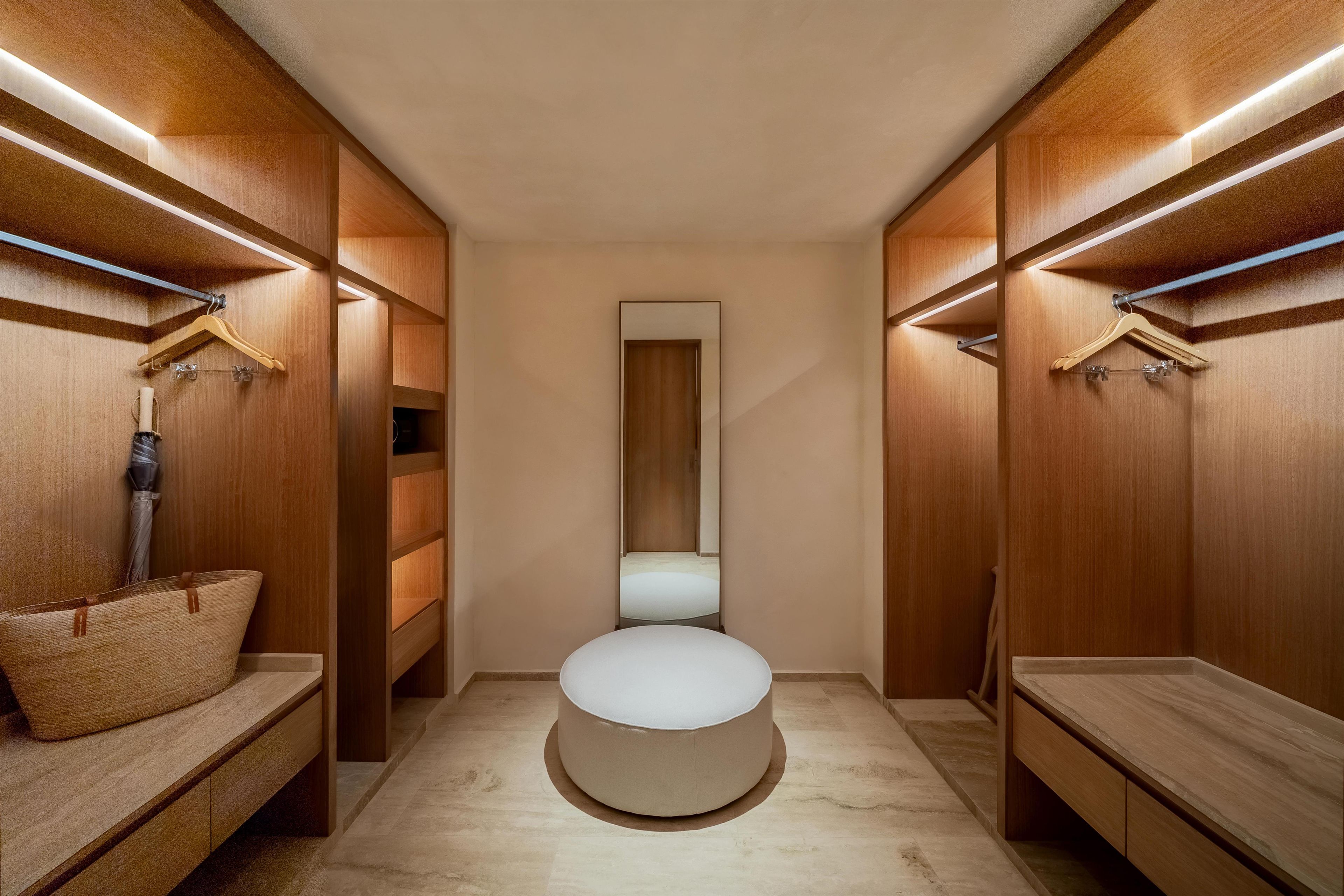 A walk-in closet with wooden shelving, a round bench, and a mirror.