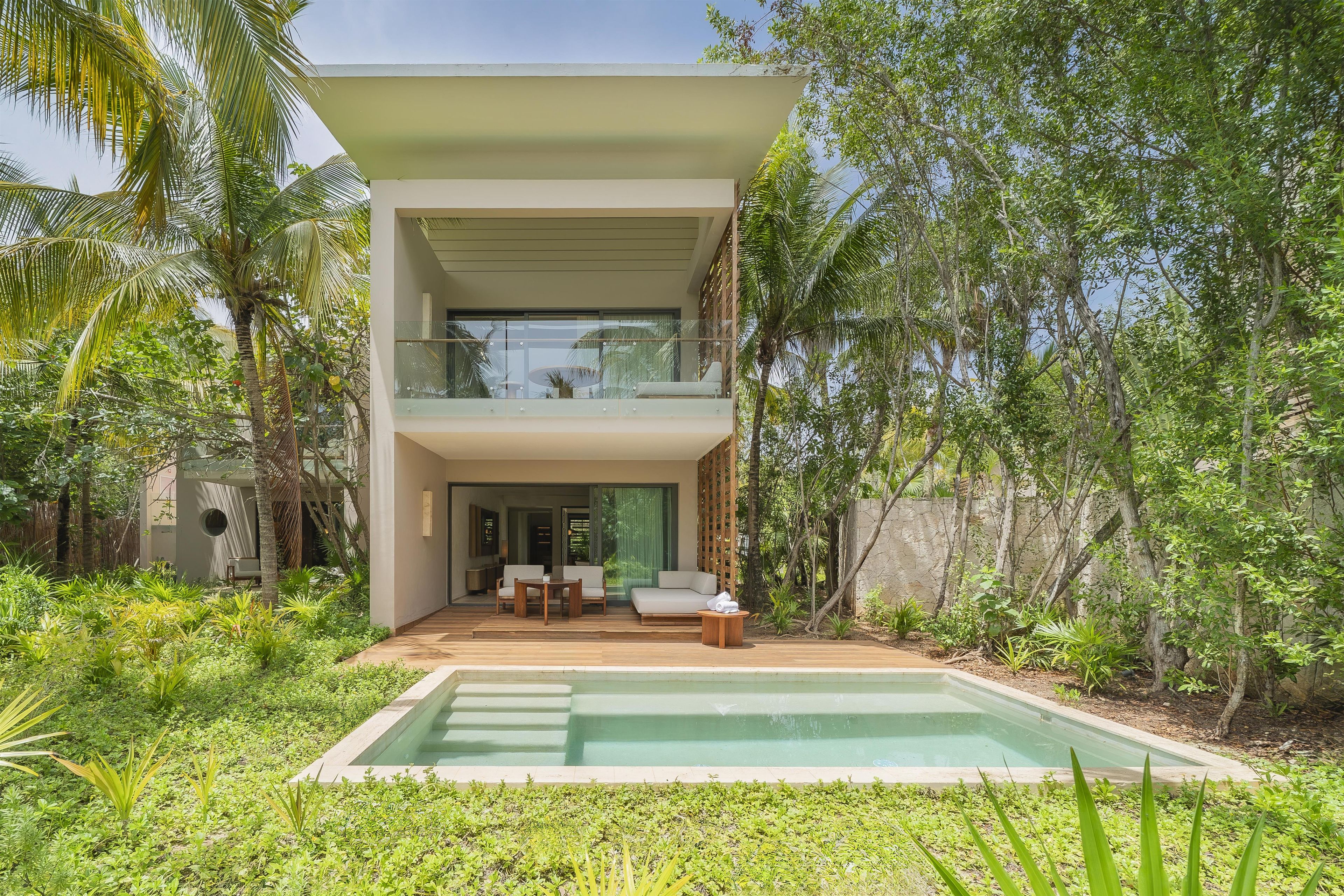 Un edificio moderno de dos pisos con piscina, rodeado de exuberante vegetación.