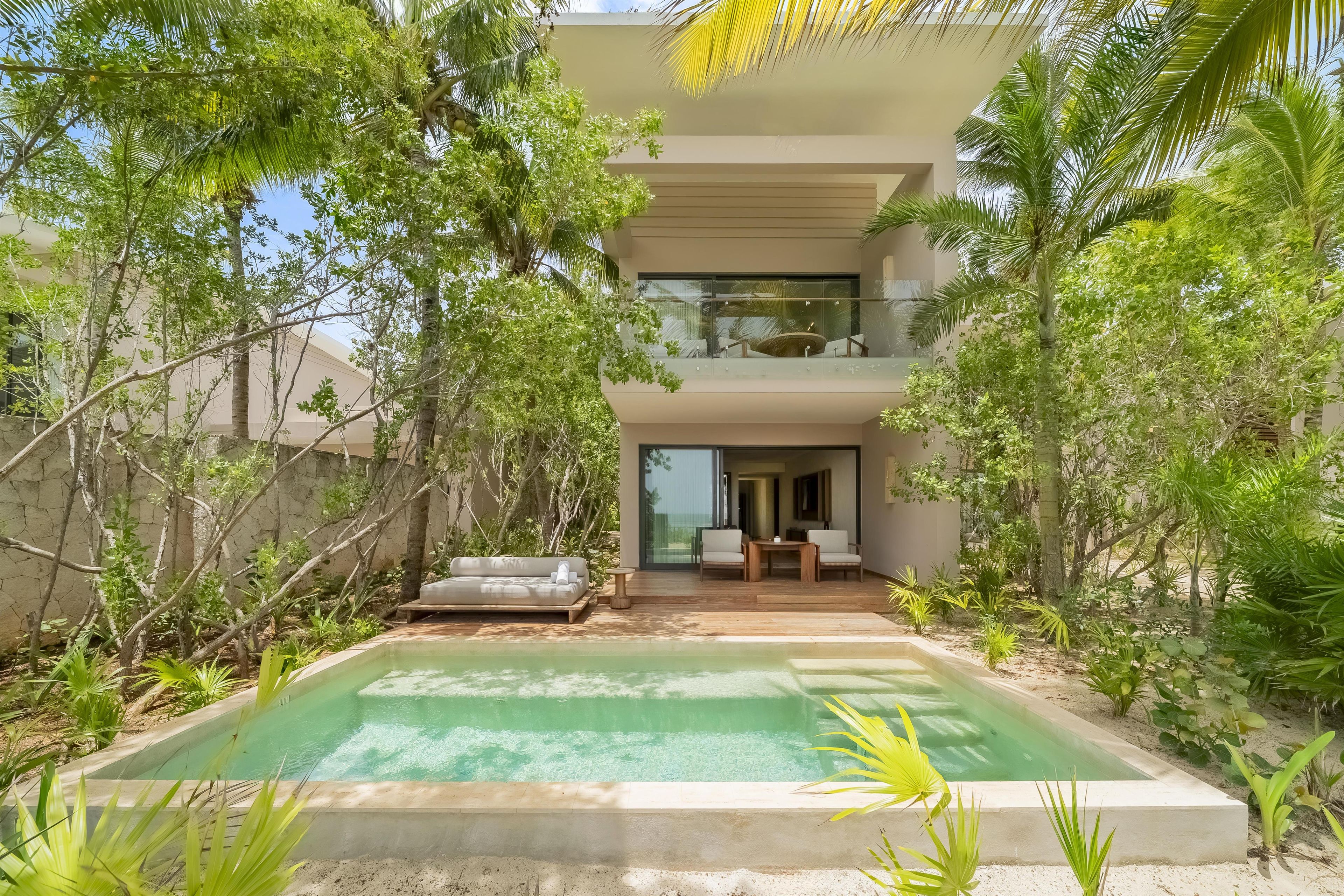 A modern two-story building with a glass balcony, a pool, and lush greenery.