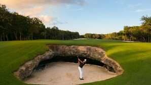 Een golfbaan met een bunker, bomen en een heldere lucht.