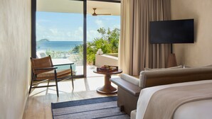 Een hotelkamer met een bed, een televisie, een stoel, een tafel met fruit en uitzicht op de oceaan.