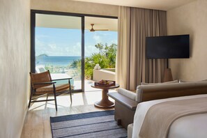 Habitación de hotel con cama, televisor, sillón, mesa con fruta y vista al océano.