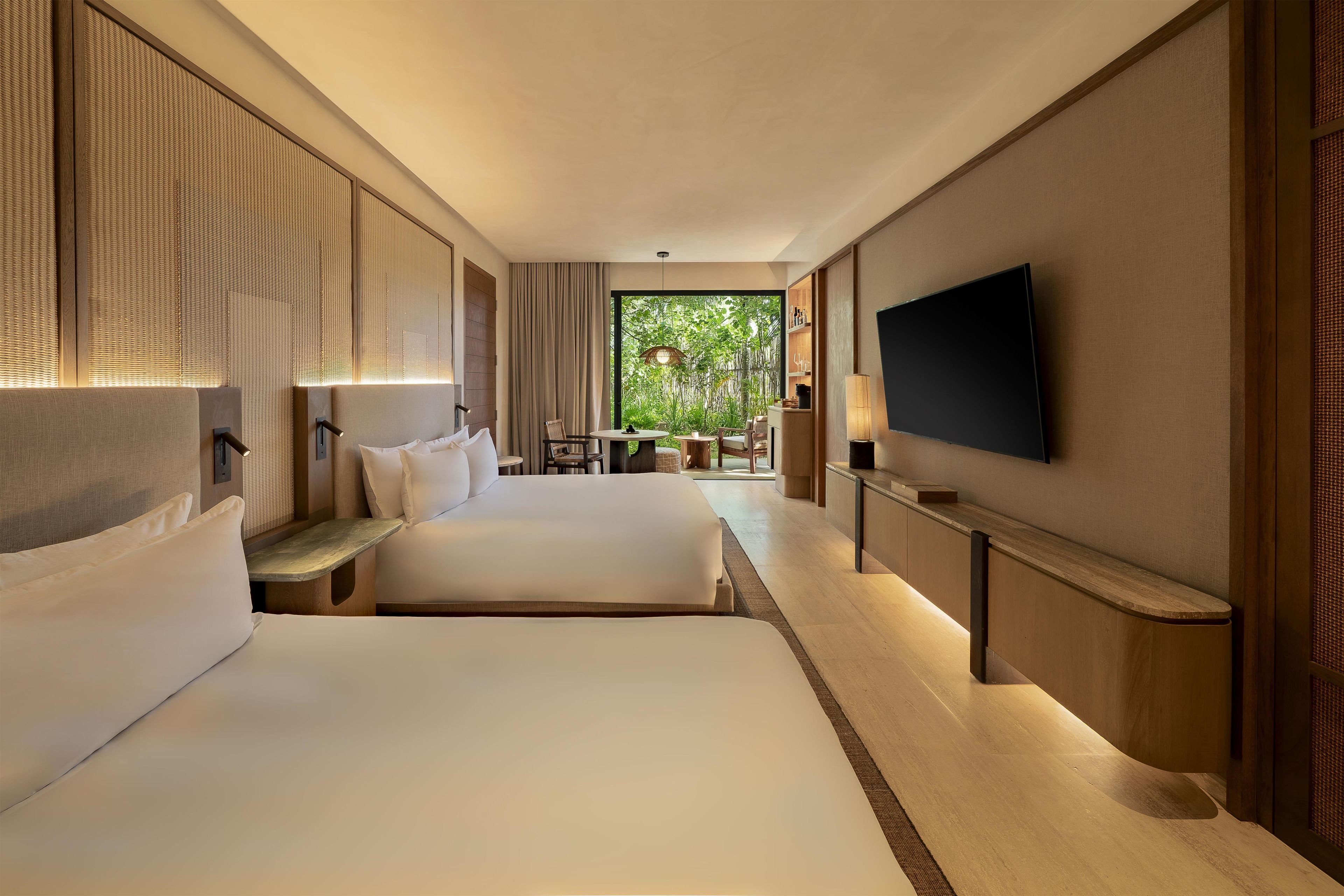 Ein Hotelzimmer mit zwei Betten, einem Fernseher und Blick auf Grünfläche.